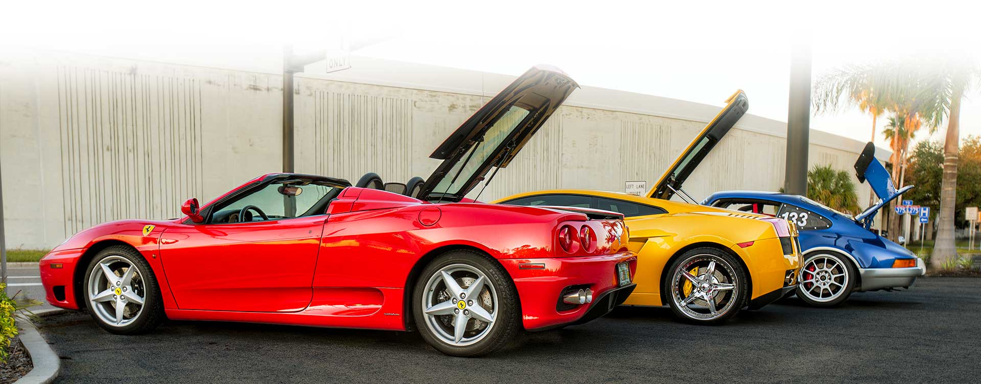 Three sports car parked outside a auto repair shop.