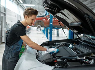 A close-up of an auto mechanic leaning on a car hood opens a car oil filter cap.