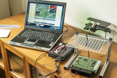 a wide shot of a laptop, electronic equipment, and a circuit board on a wooden table.