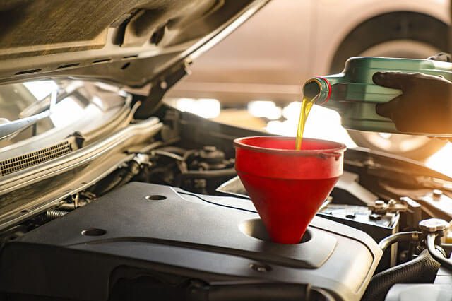 A close-up of a man pouring new oil into a car oil filter using a red funnel.
