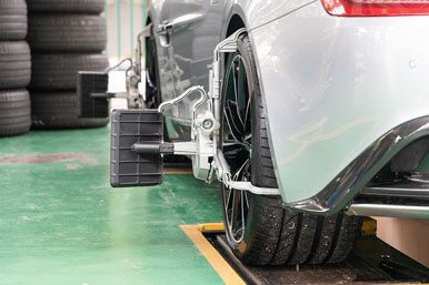 A close-up if a white car with a wheel alignment attach to rear tire.