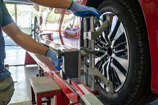 A close-up of an auto mechanic doing a wheel alignment repair on a car on a car lift.
